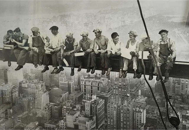 “Lunch atop a Skyscraper,” which depicts construction workers eating lunch on a steel beam high above New York City, taken in 1932 during the construction of the RCA Building at Rockefeller Center. The photograph has been attributed to Charles C. Ebbets, though there has been some debate over the years about who exactly took the photograph due to the lack of clear documentation. It remains an iconic image of the American spirit during the Great Depression.